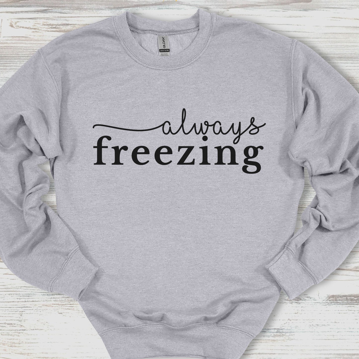 Gray sweatshirt with 'always freezing' text on a wooden surface
