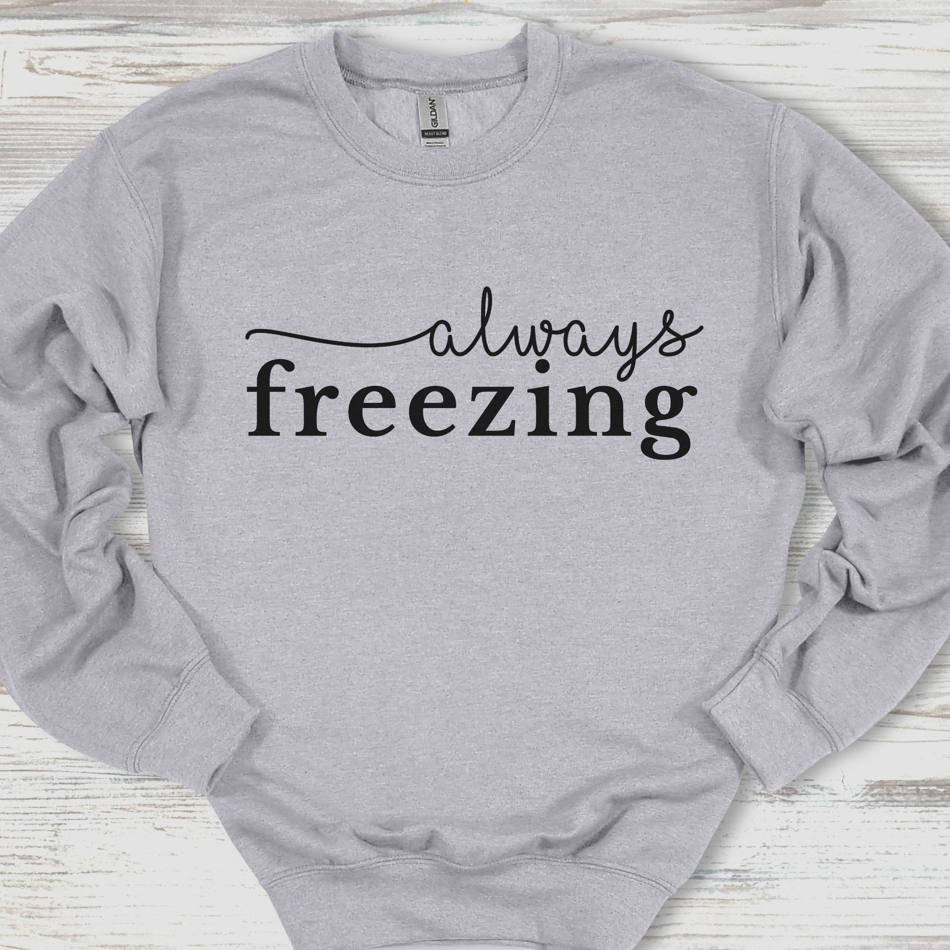 Gray sweatshirt with 'always freezing' text on a wooden surface