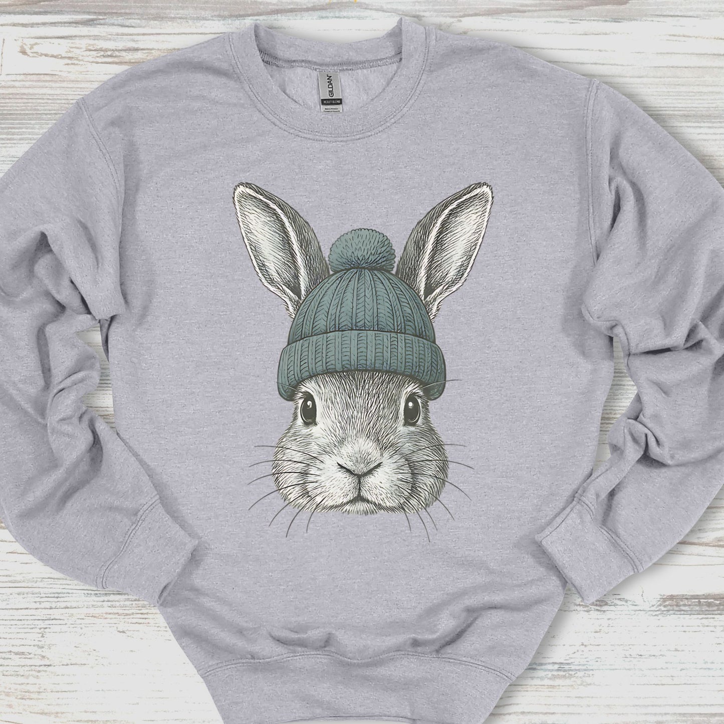 Gray sweatshirt with a graphic of a rabbit wearing a green beanie on a wooden surface