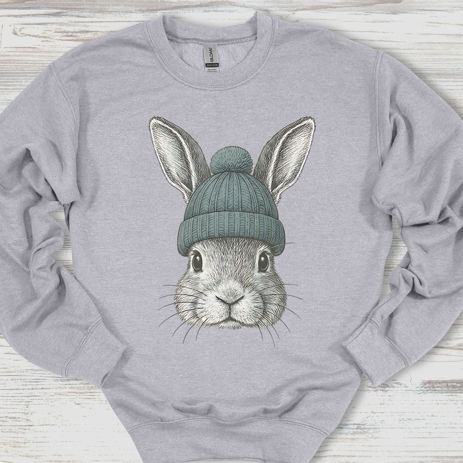 Gray sweatshirt with a graphic of a rabbit wearing a green beanie on a wooden surface