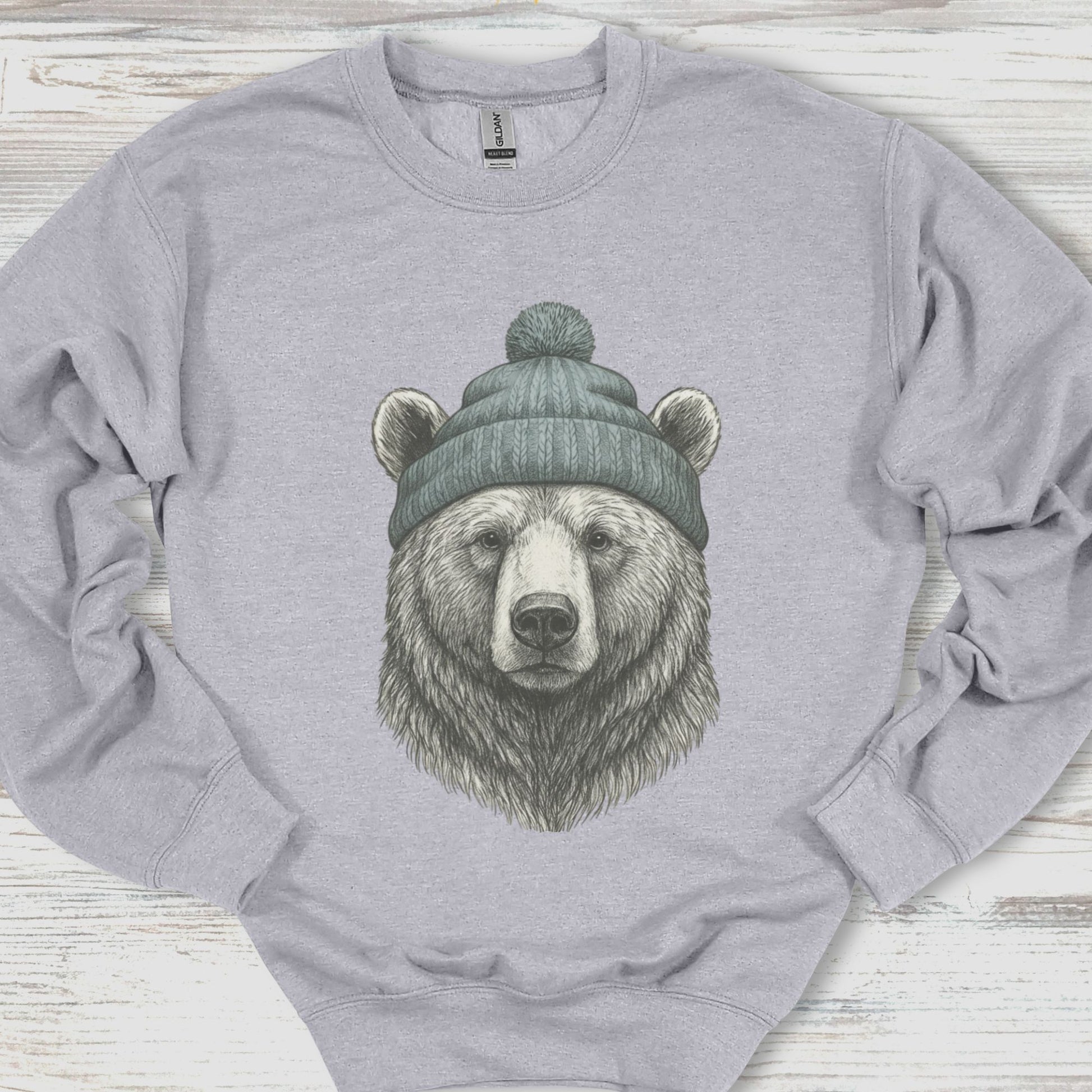 Gray sweatshirt with a bear wearing a beanie on a wooden surface