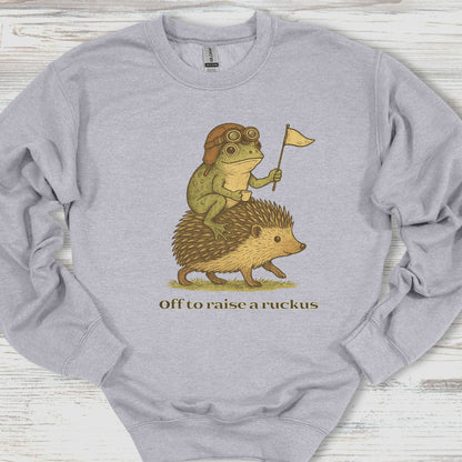 Gray sweatshirt with a graphic of a frog riding a hedgehog and text 'Off to raise a ruckus' on a wooden surface.