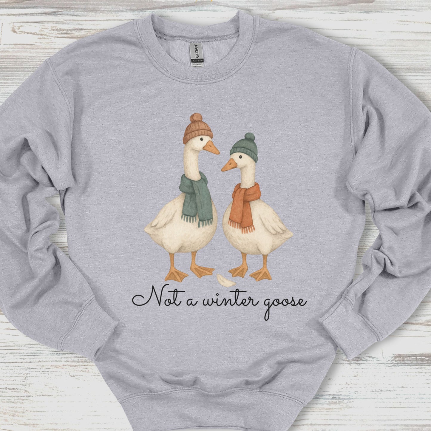 Gray sweatshirt with two geese wearing hats and scarves, and text 'Not a winter goose' on a wooden surface.