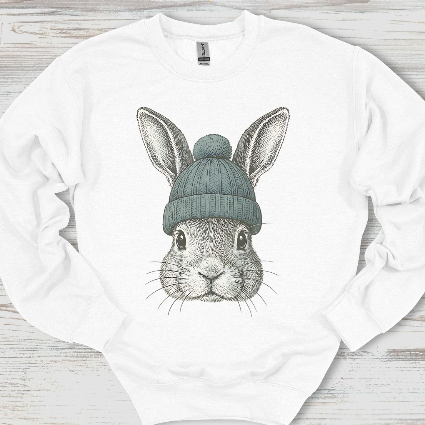 White sweatshirt with a graphic of a rabbit wearing a green beanie on a wooden surface