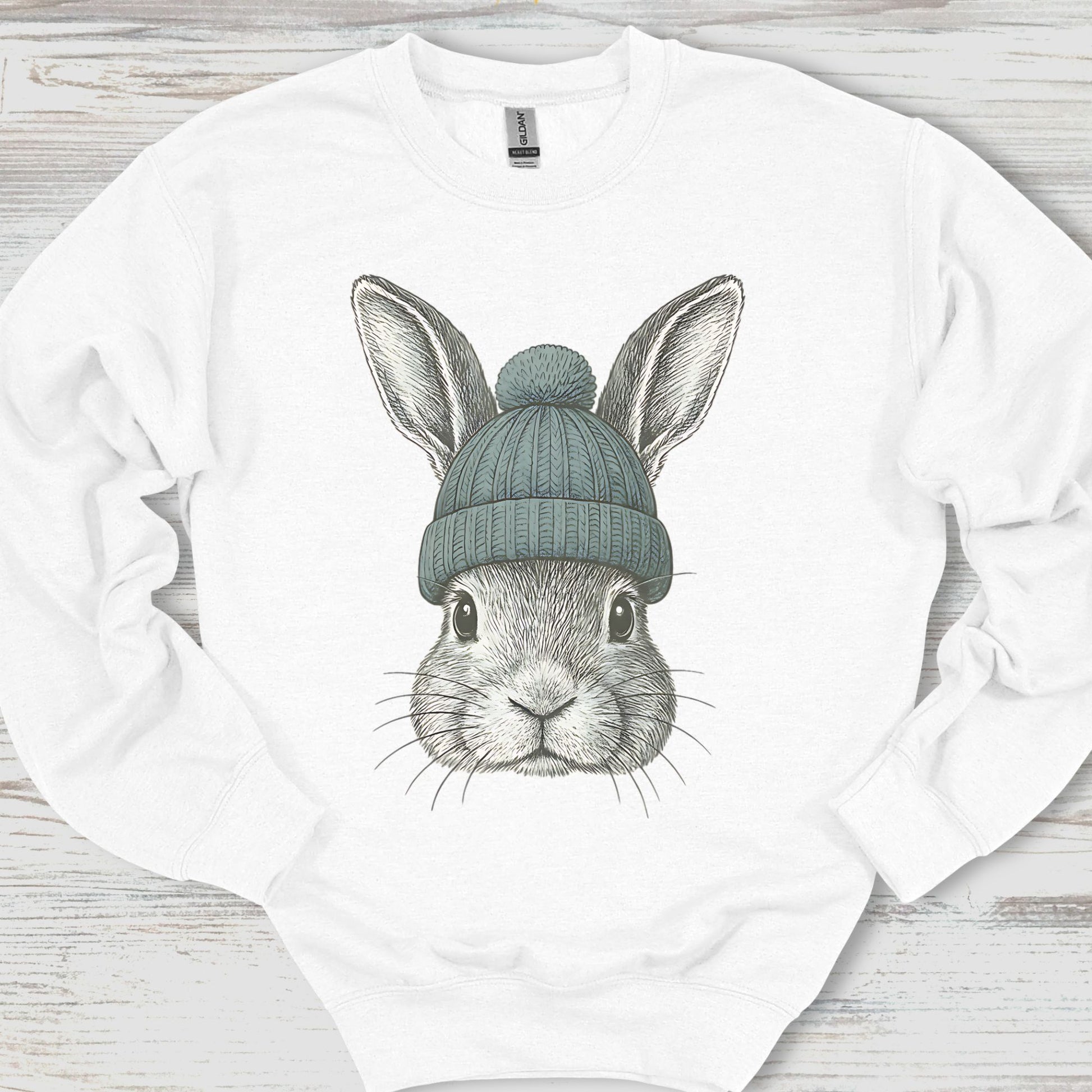 White sweatshirt with a graphic of a rabbit wearing a green beanie on a wooden surface