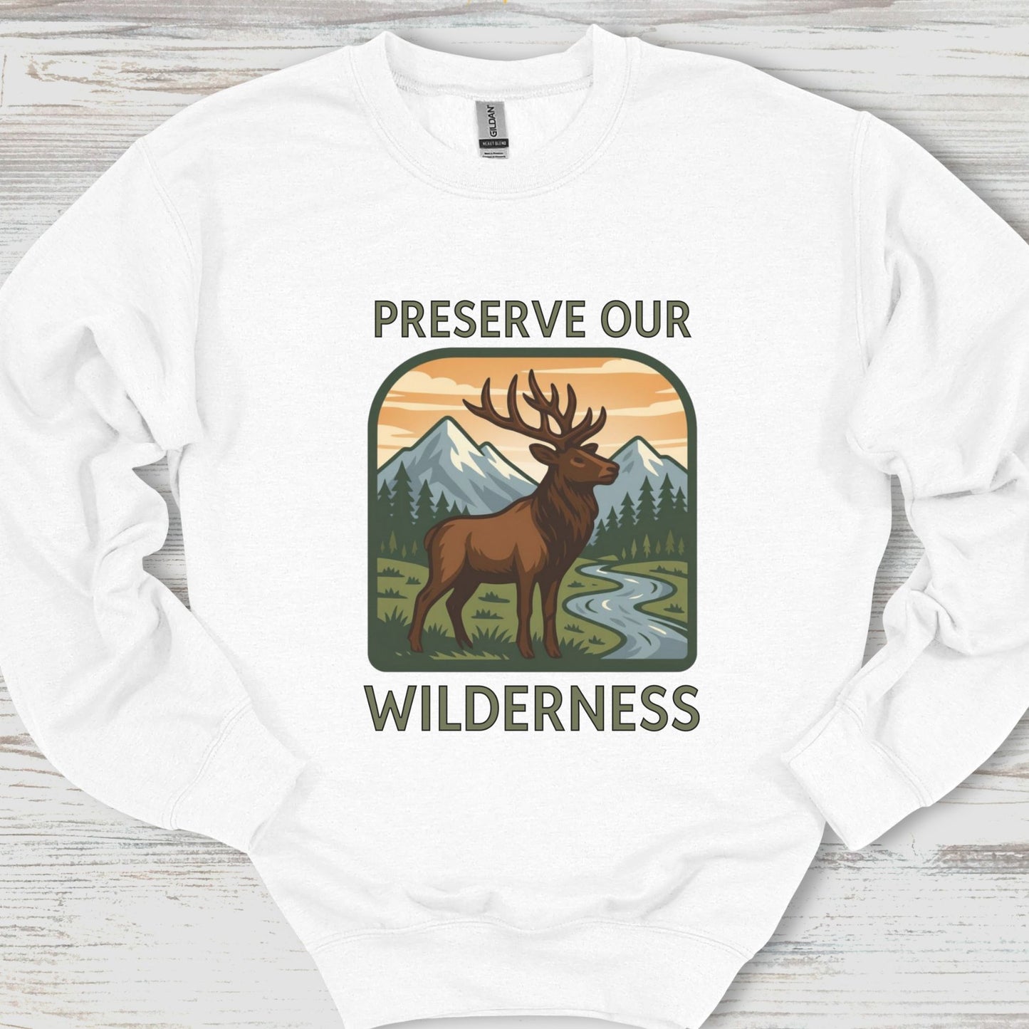 White sweatshirt with a graphic of a deer and mountains and text 'Preserve Our Wilderness' on a wooden surface.