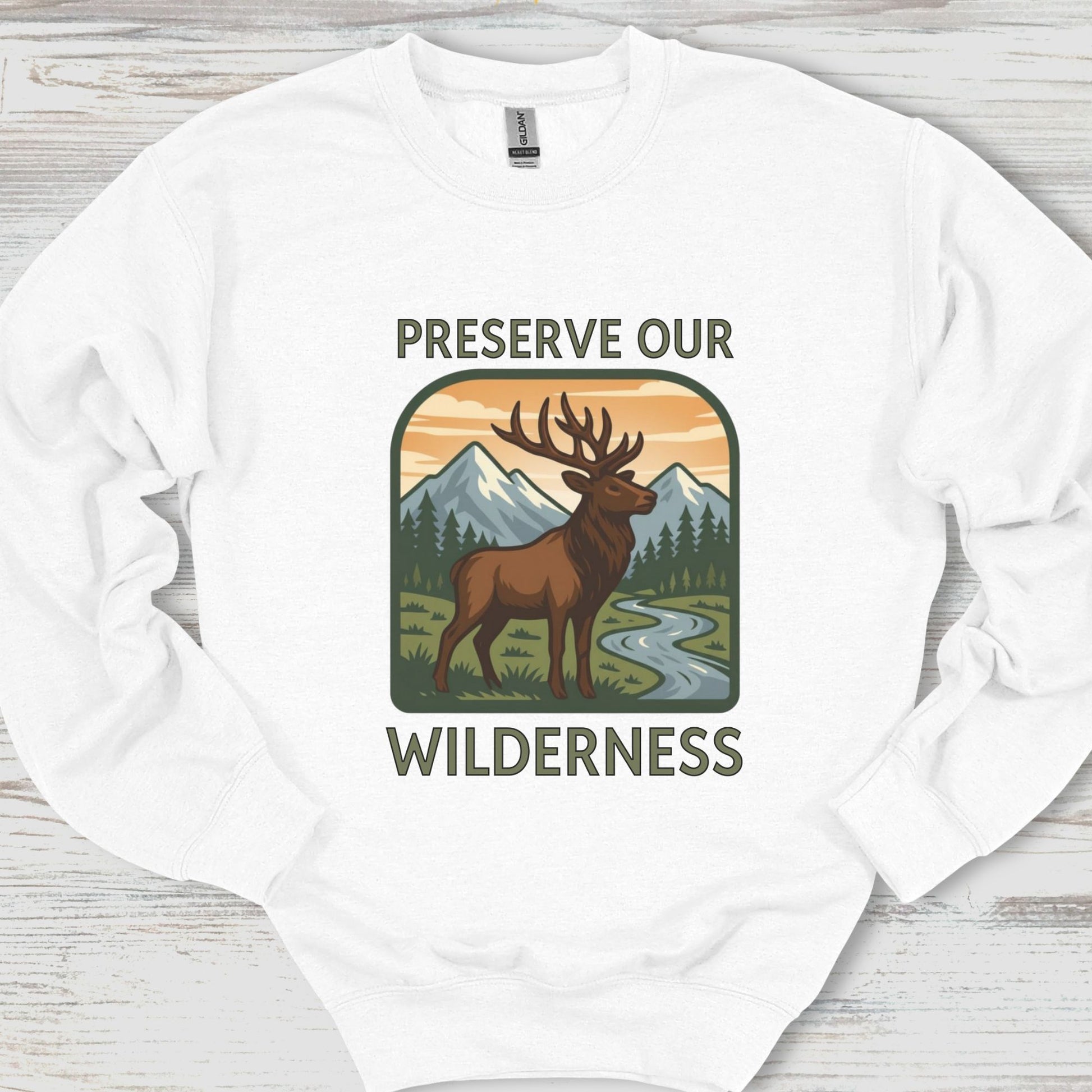 White sweatshirt with a graphic of a deer and mountains and text 'Preserve Our Wilderness' on a wooden surface.