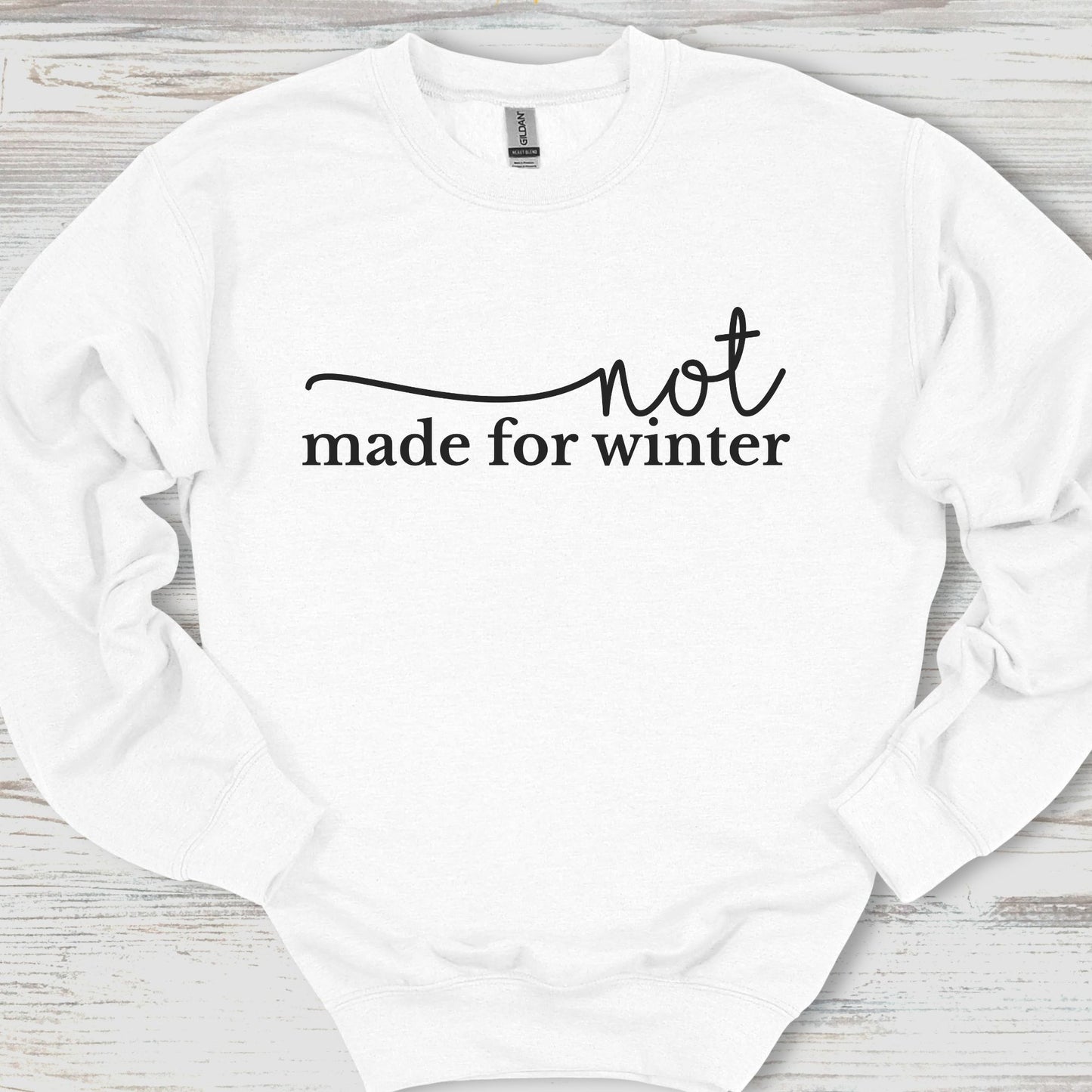 White sweatshirt with 'not made for winter' text on a wooden surface