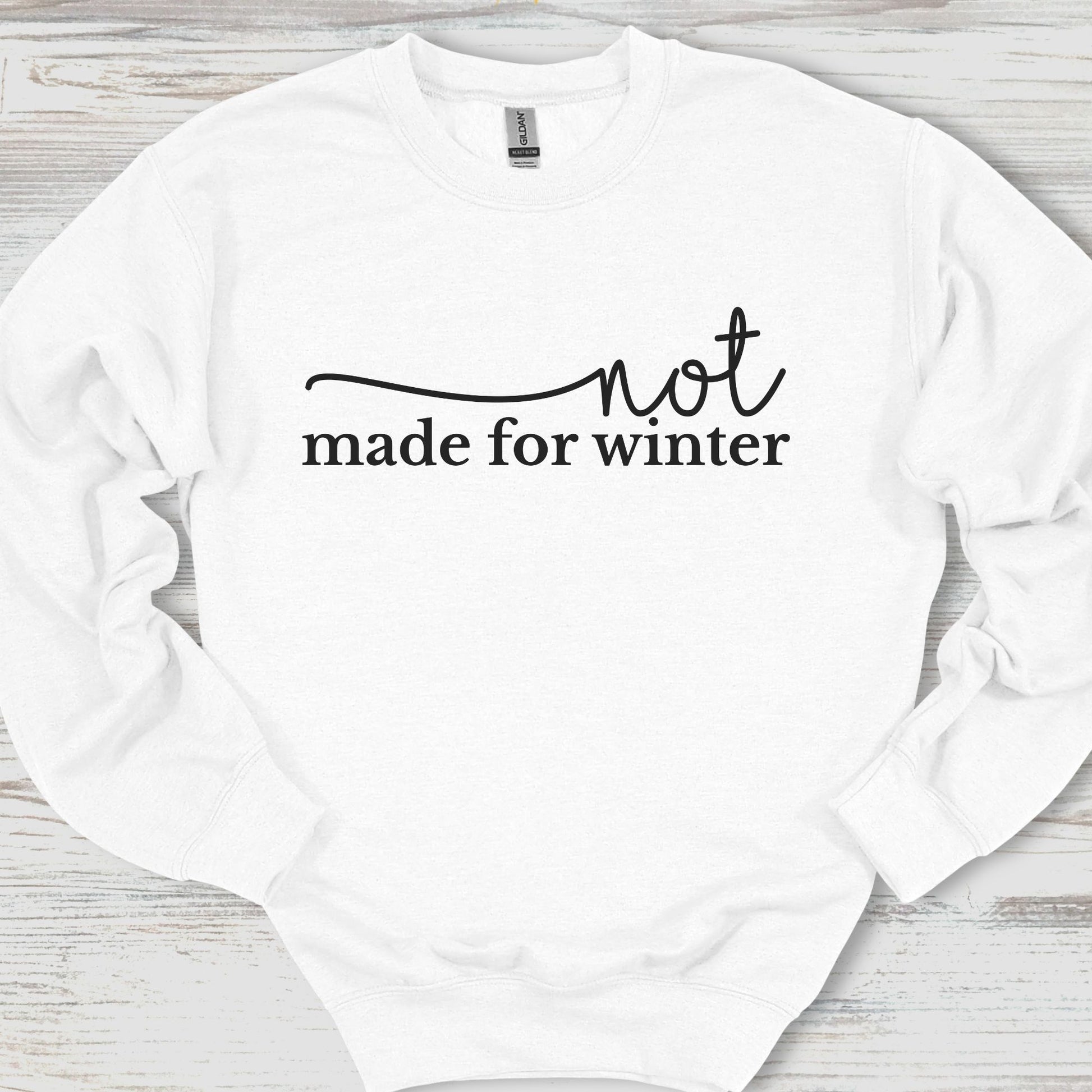 White sweatshirt with 'not made for winter' text on a wooden surface