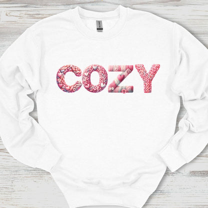 White sweatshirt with 'COZY' printed in pink letters on a wooden surface