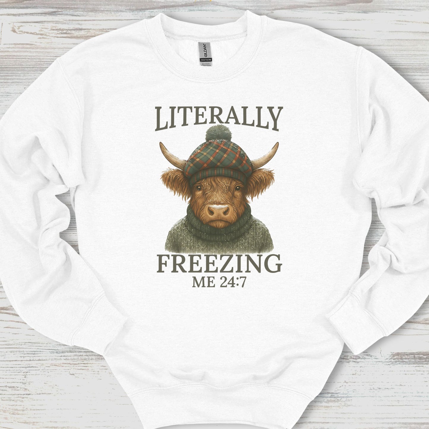 White sweatshirt with a highland cow graphic and text on a wooden surface