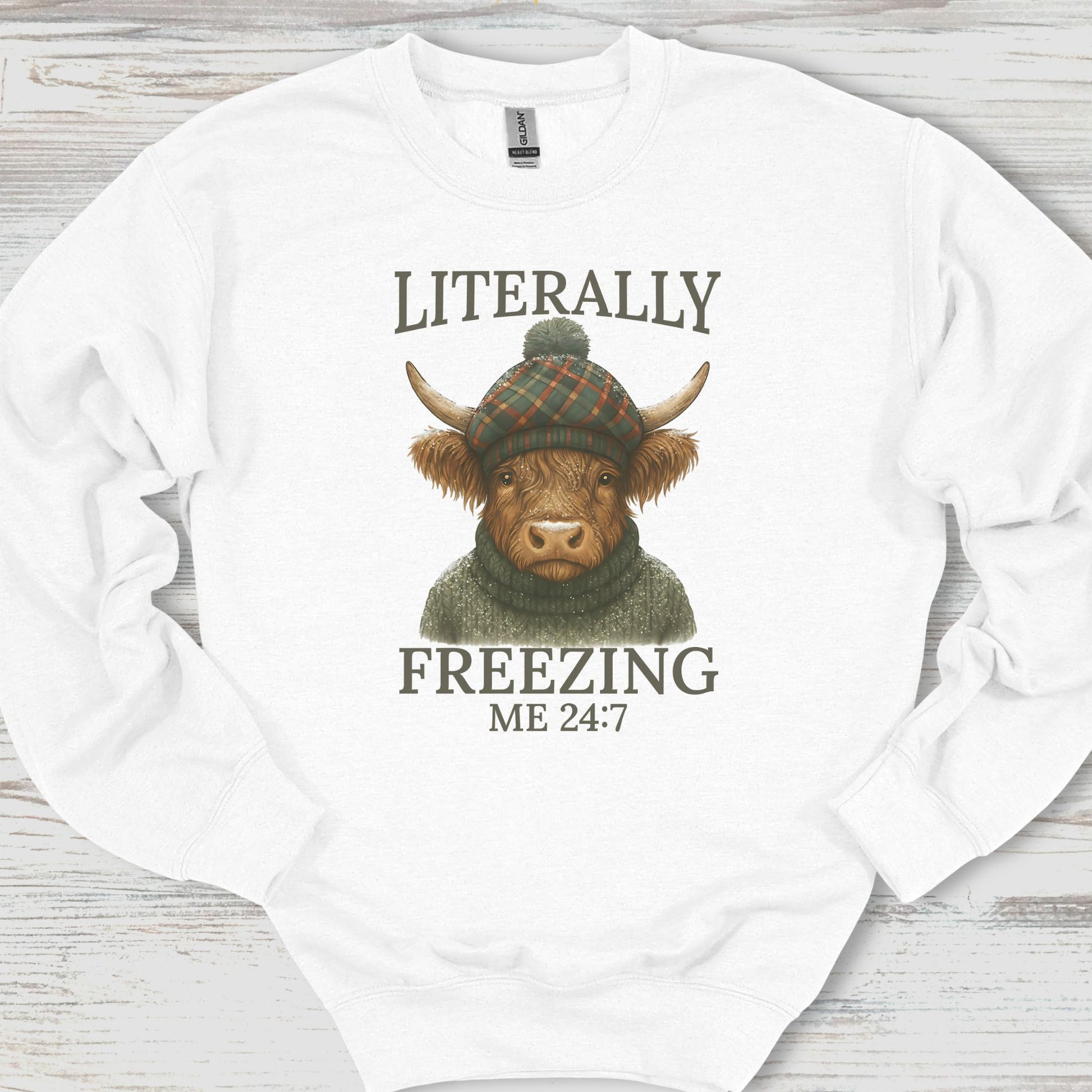 White sweatshirt with a highland cow graphic and text on a wooden surface