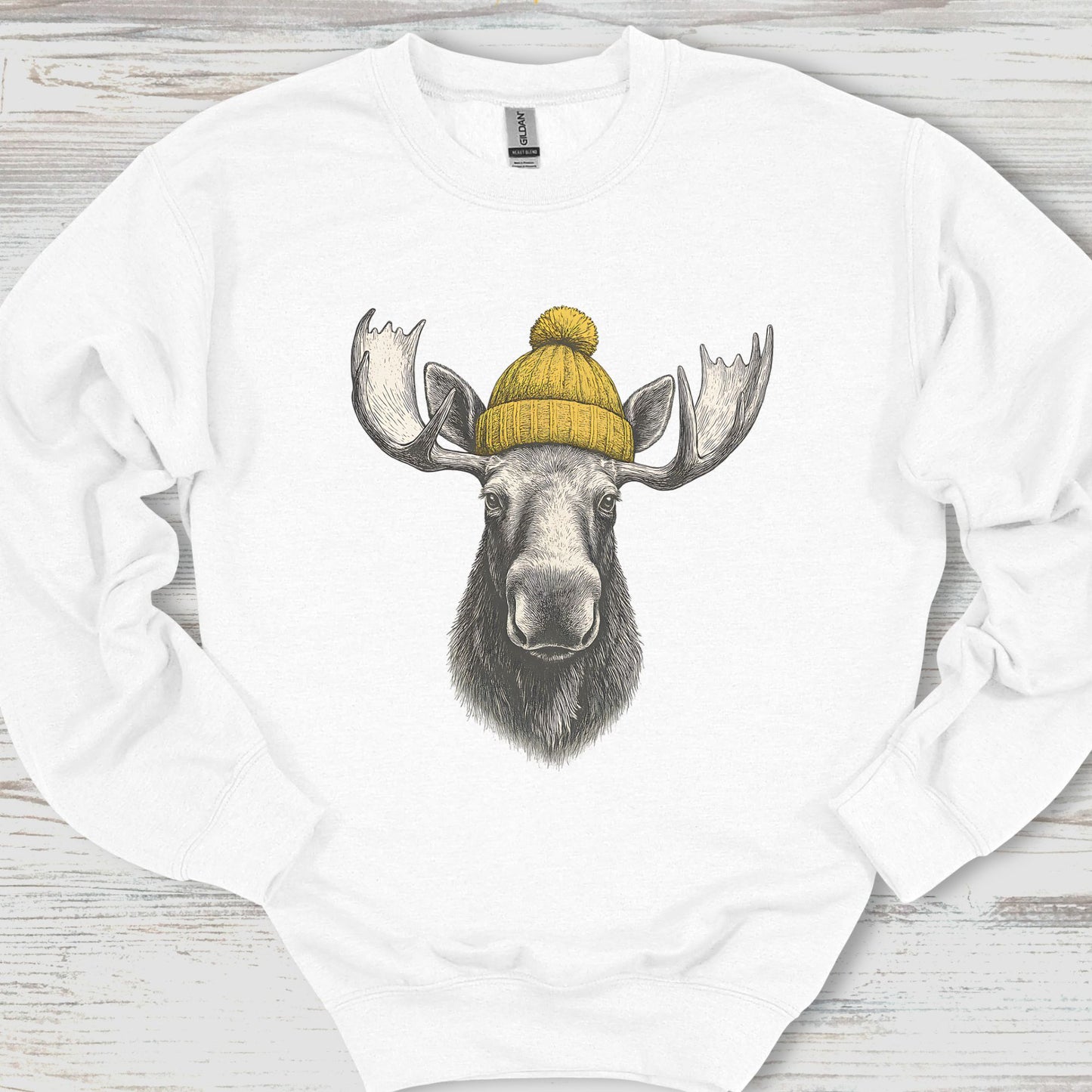 White sweatshirt with a moose wearing a yellow beanie on a wooden surface
