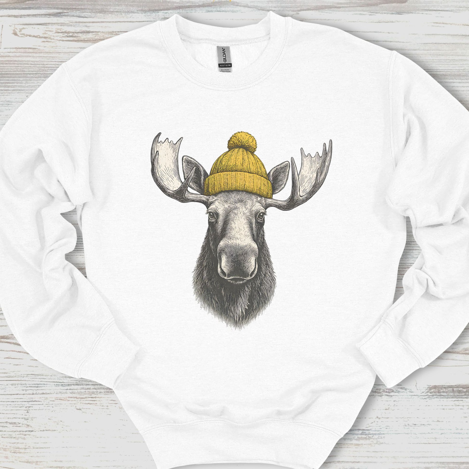 White sweatshirt with a moose wearing a yellow beanie on a wooden surface