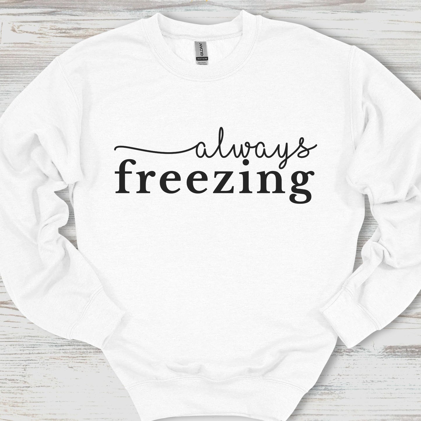 White sweatshirt with 'always freezing' text on a wooden surface