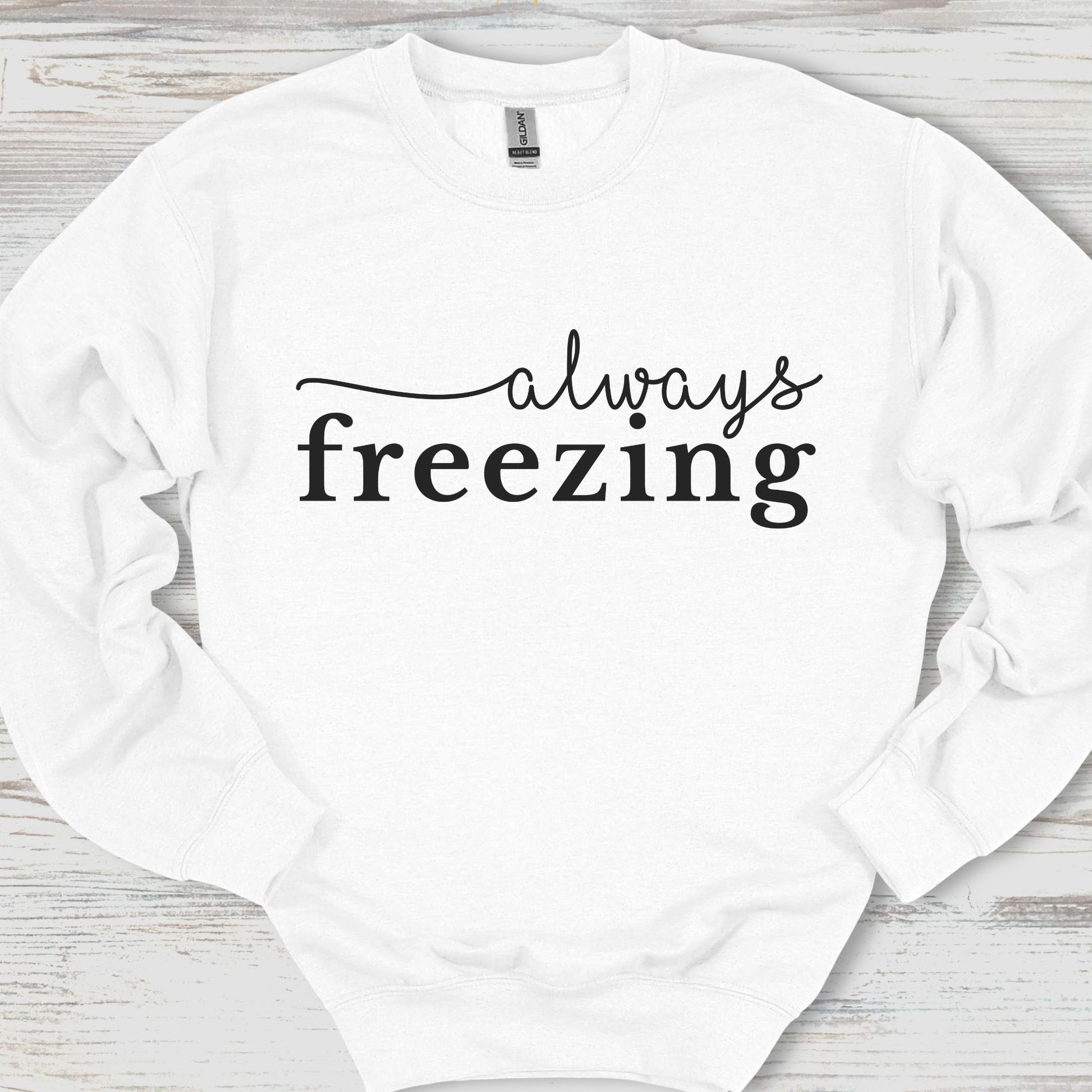 White sweatshirt with 'always freezing' text on a wooden surface