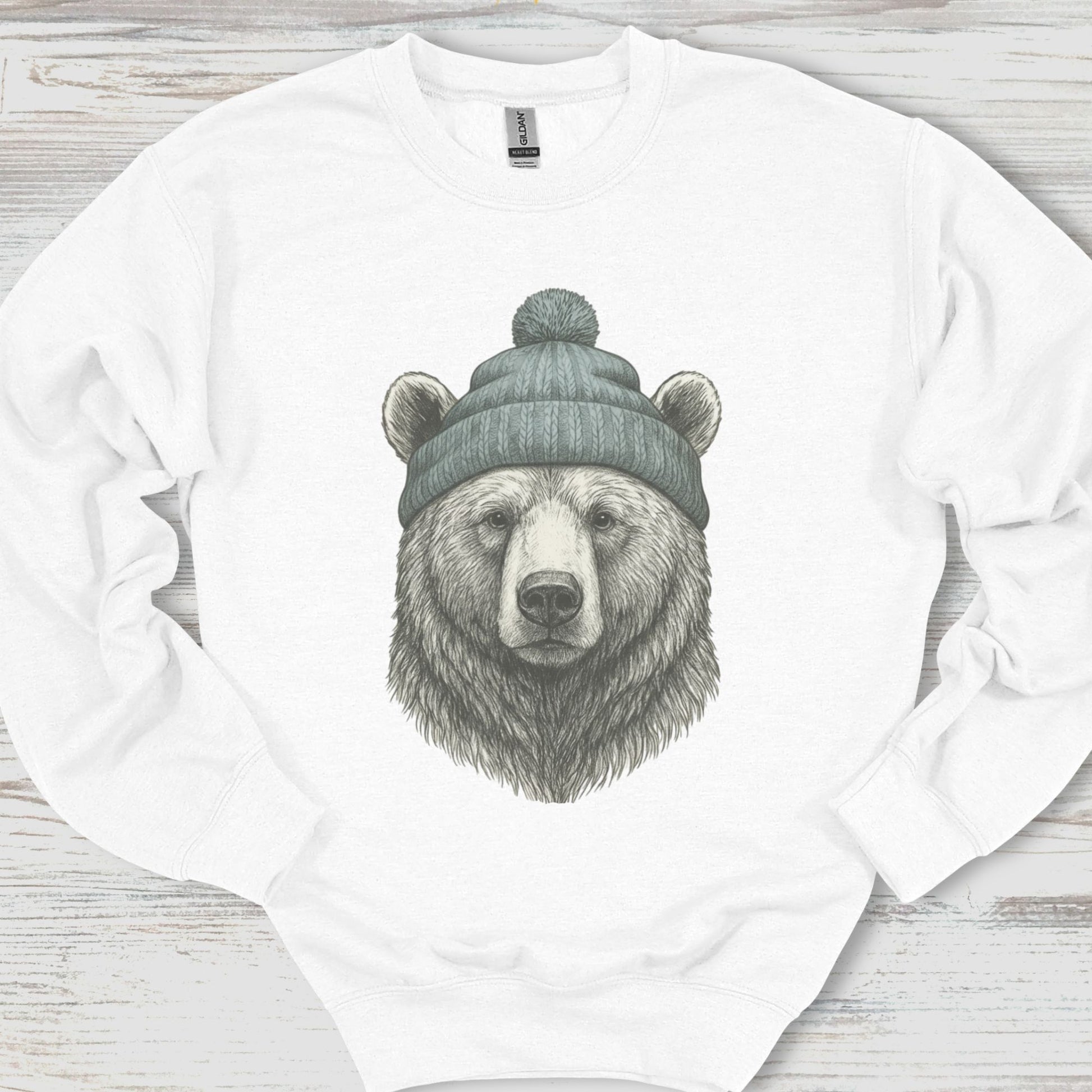 White sweatshirt with a bear wearing a beanie design on a wooden surface