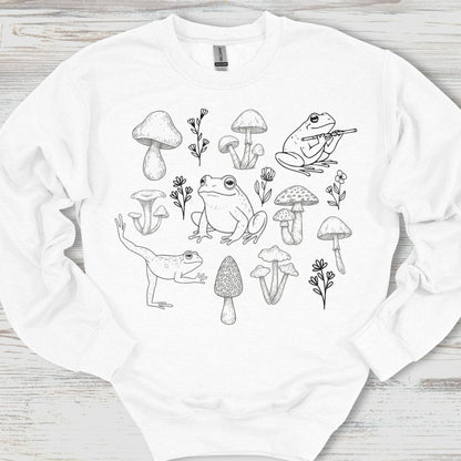 White sweatshirt with black line art design of frogs and mushrooms on a wooden surface