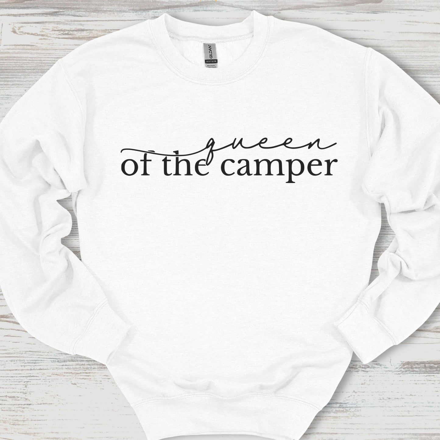 White sweatshirt with 'queen of the camper' text on a wooden surface