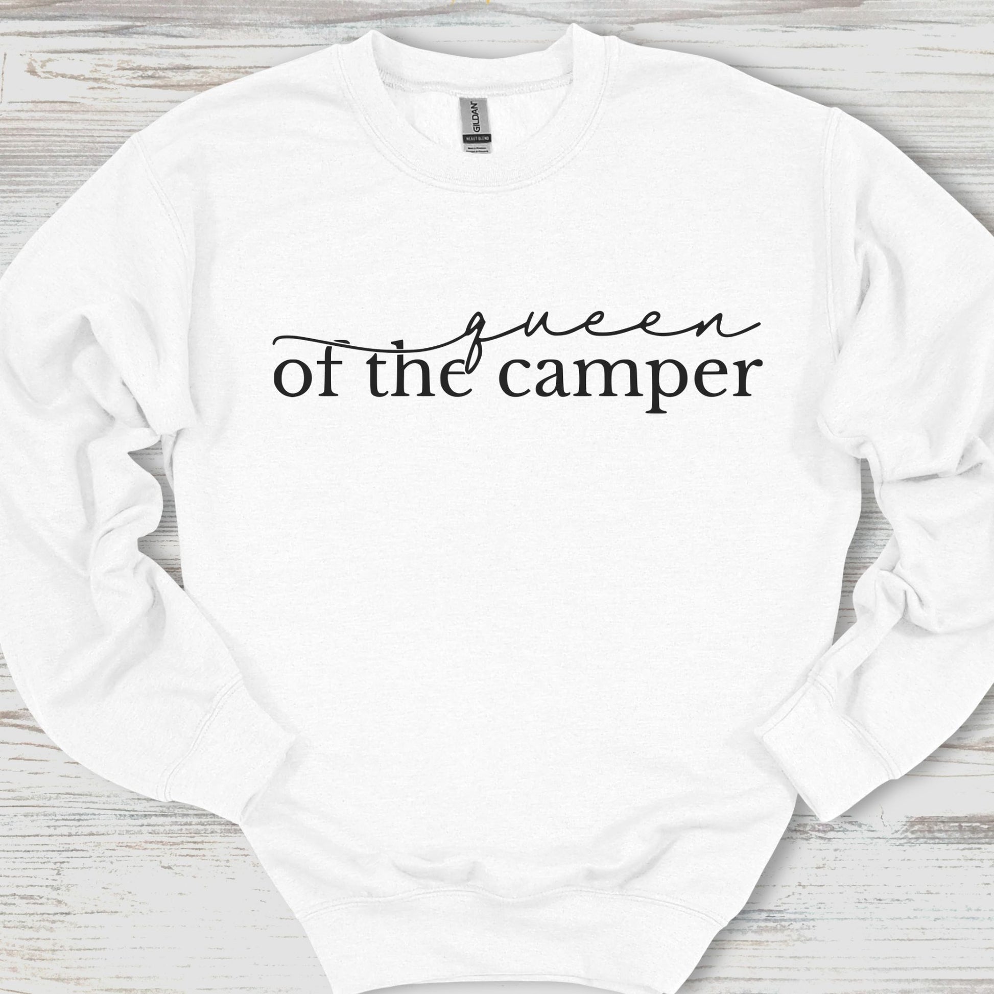 White sweatshirt with 'queen of the camper' text on a wooden surface