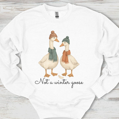 White sweatshirt with two cartoon geese wearing hats and scarves, and text 'Not a winter goose' on a wooden surface.