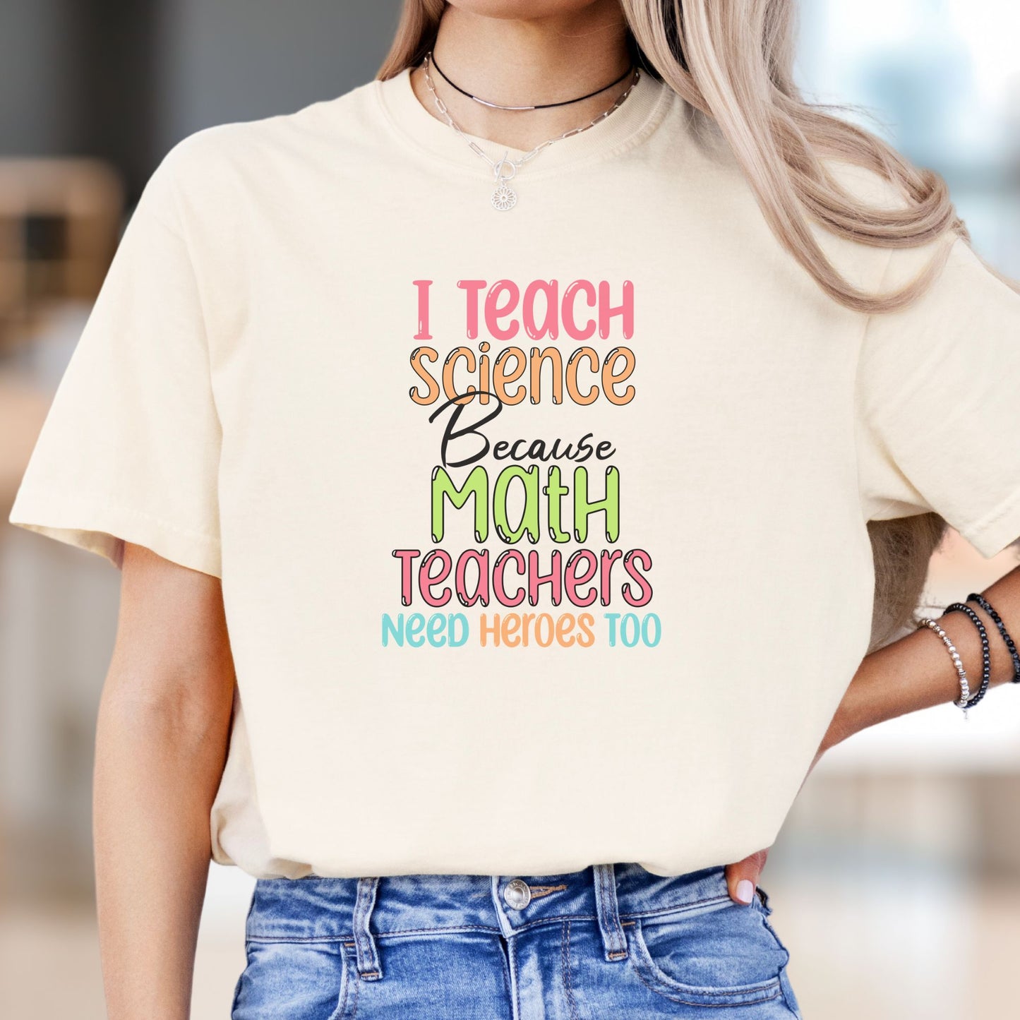 Model wears a black tshirt with lettering in fun chunky lettering in pastel rainbow colors that reads, I Teach Science Because Math Teachers need Heroes Too.. Makes a great give for a Science Teacher