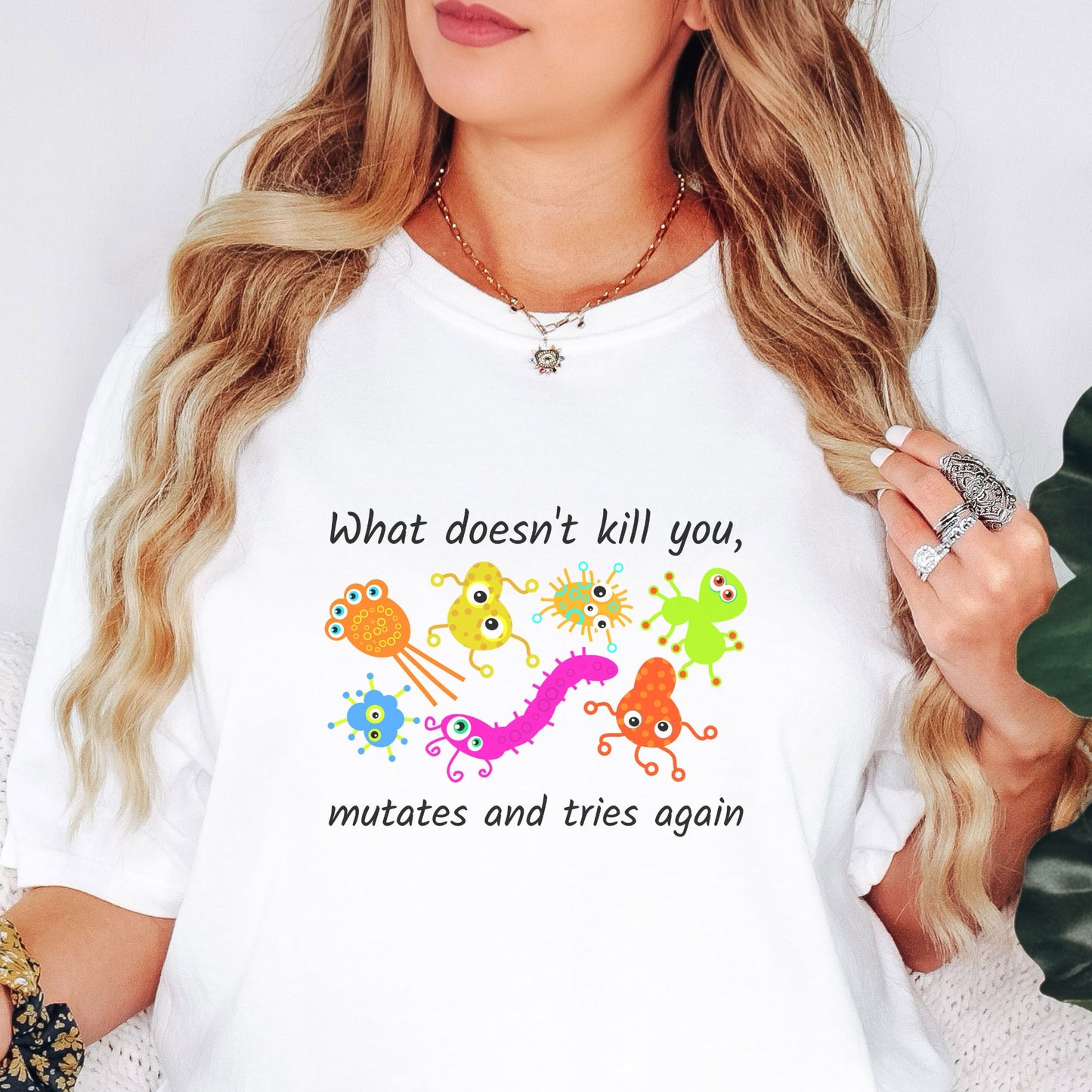 Model wears a white tshirt with colorful hand drawn virus characters. The black lettering reads, What doesn't kill you, mutates and tries again.  This is a great gift for a science teacher or biology lover.